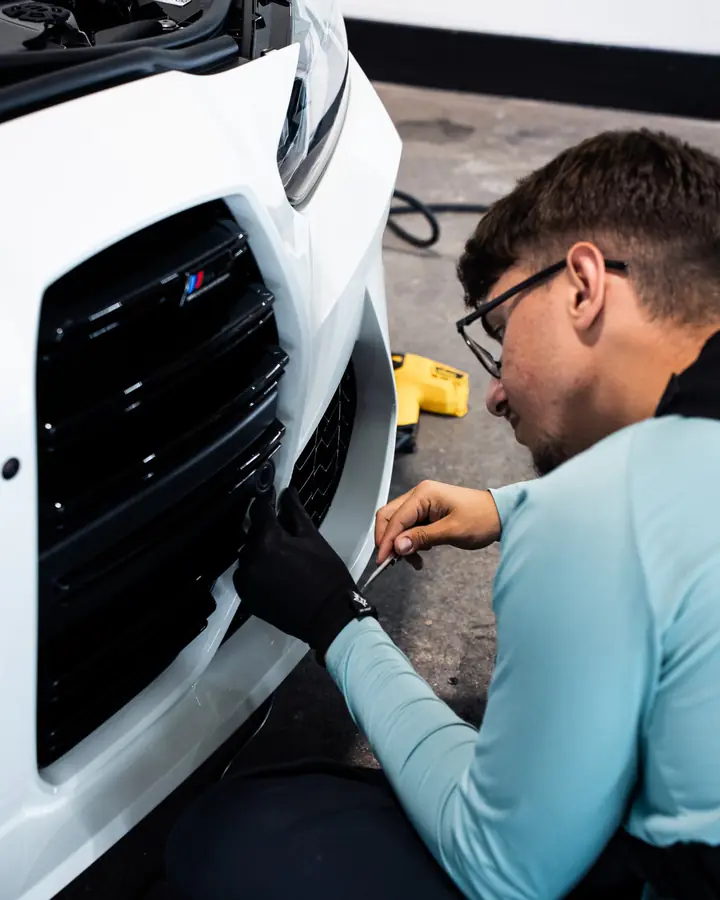 Technician applying paint protection film around the front grille of a white BMW