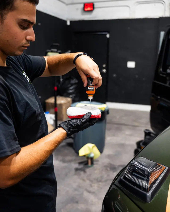 Technician pouring ceramic coating onto an applicator pad beside a green Mercedes G-Class