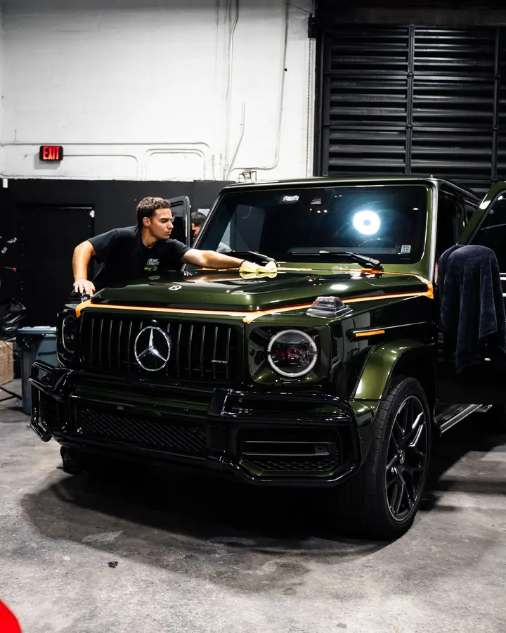 Technician buffing ceramic coating on the hood of a green Mercedes G-Class