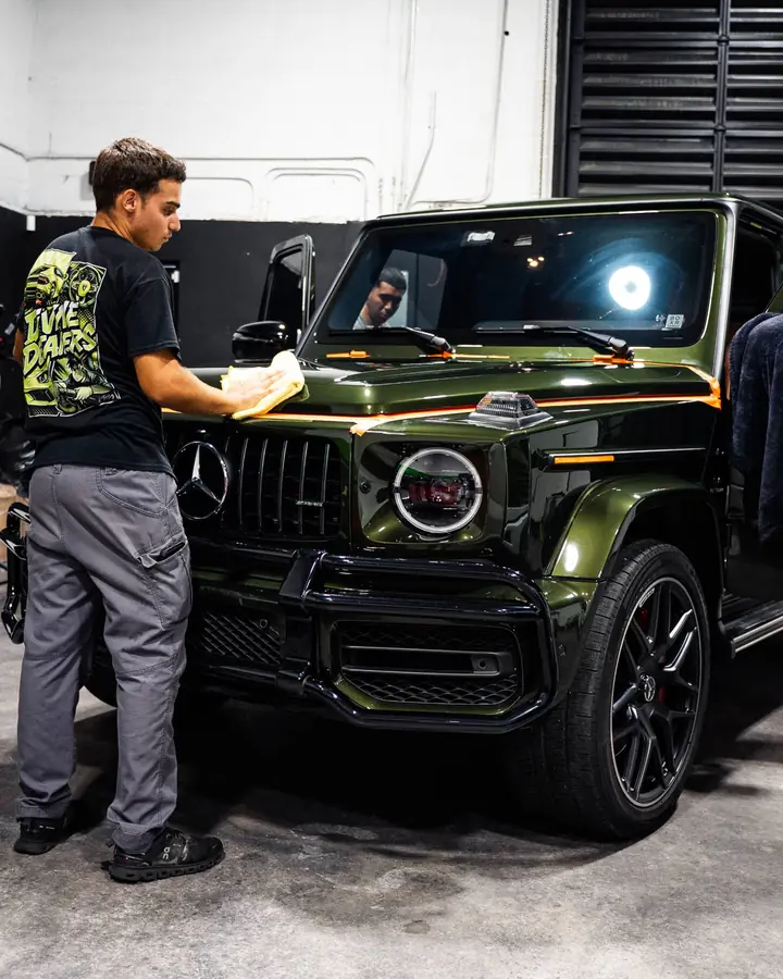 Technician wiping the hood of a green Mercedes G-Class after ceramic coating