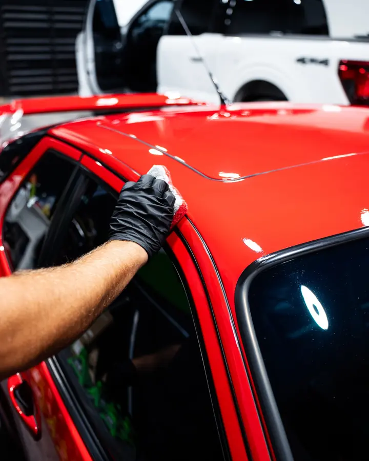 Gloved hand applying ceramic coating along the roof edge of a red car
