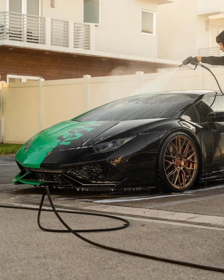 Technician pressure washing a green and black Lamborghini Huracan with foam