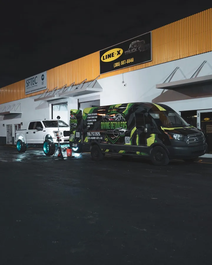 Lifted white Ford F-150 parked beside the Divine Detailers wrapped mobile detailing van at night