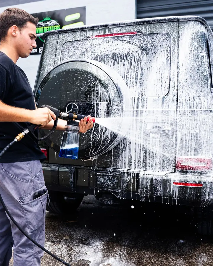 Technician foam washing a green Mercedes G-Class outside the shop