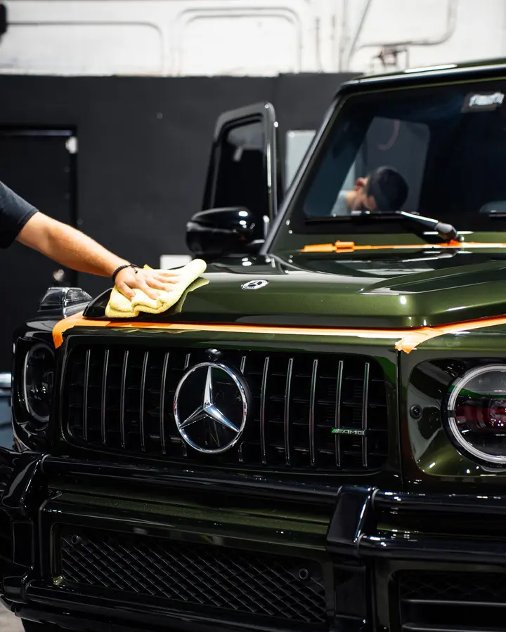 Technician wiping the hood of a green Mercedes G-Class with a microfiber towel
