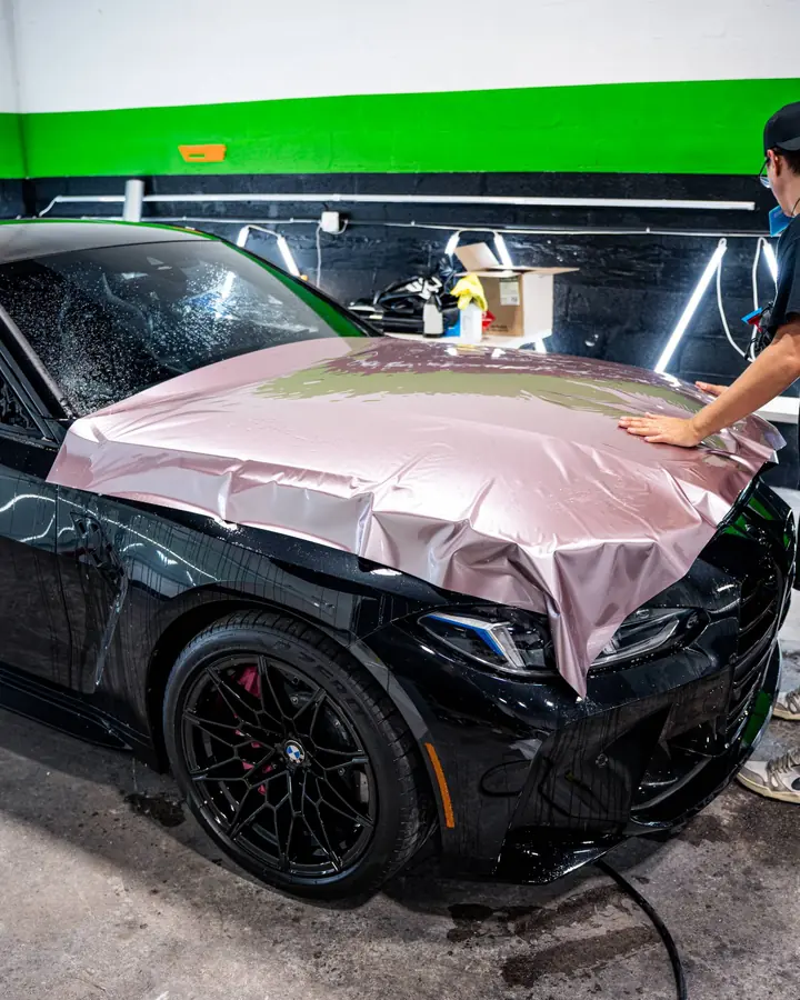 Pink color film being laid over the hood of a black BMW M3