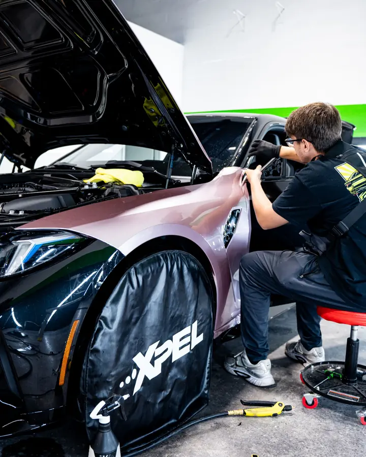 Technician finishing film on the pink fender of a BMW M3 next to an XPEL wheel cover