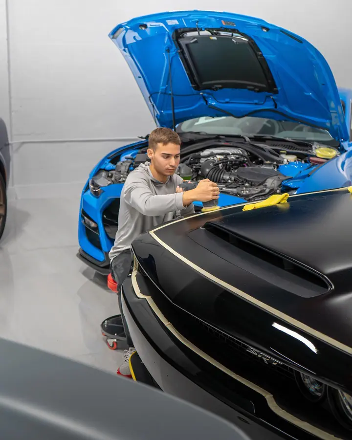 Technician machine polishing the masked hood of a black Dodge Challenger SRT in the shop