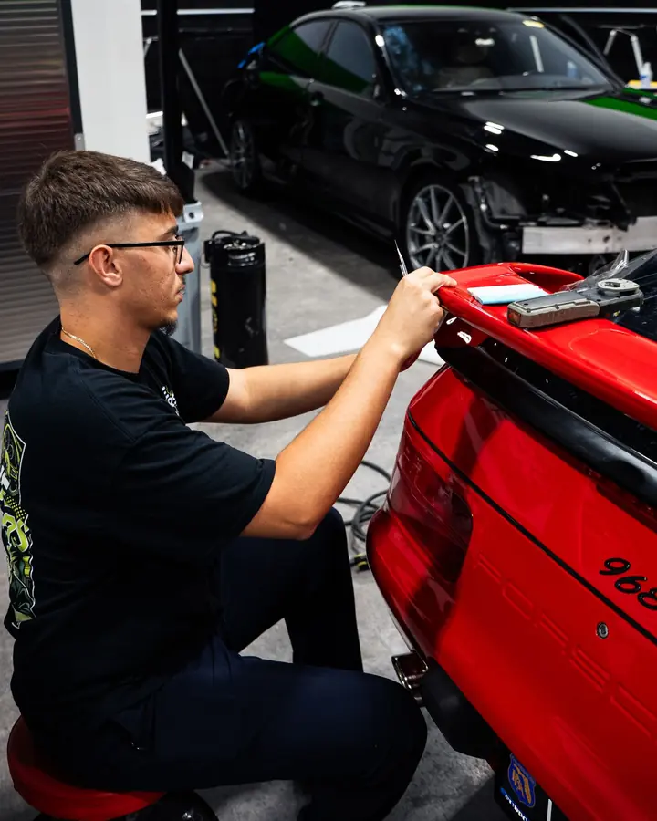 Technician applying paint protection film to the rear spoiler of a red Porsche 968