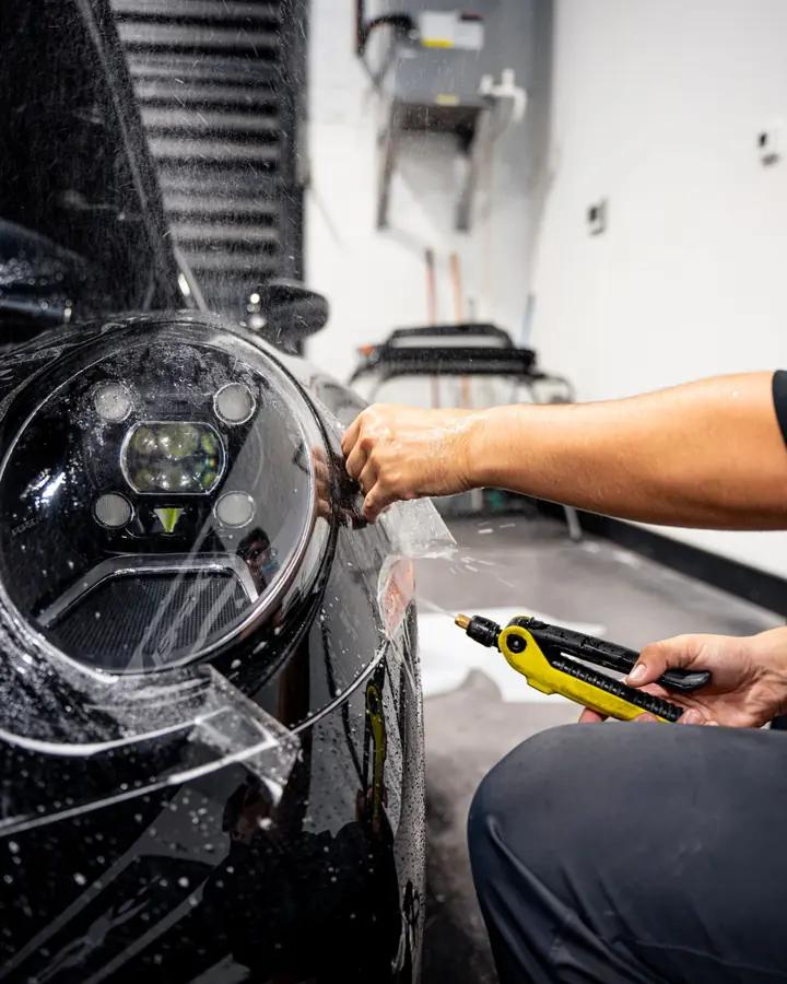 Technician spraying water and lifting paint protection film around the headlight of a black Porsche
