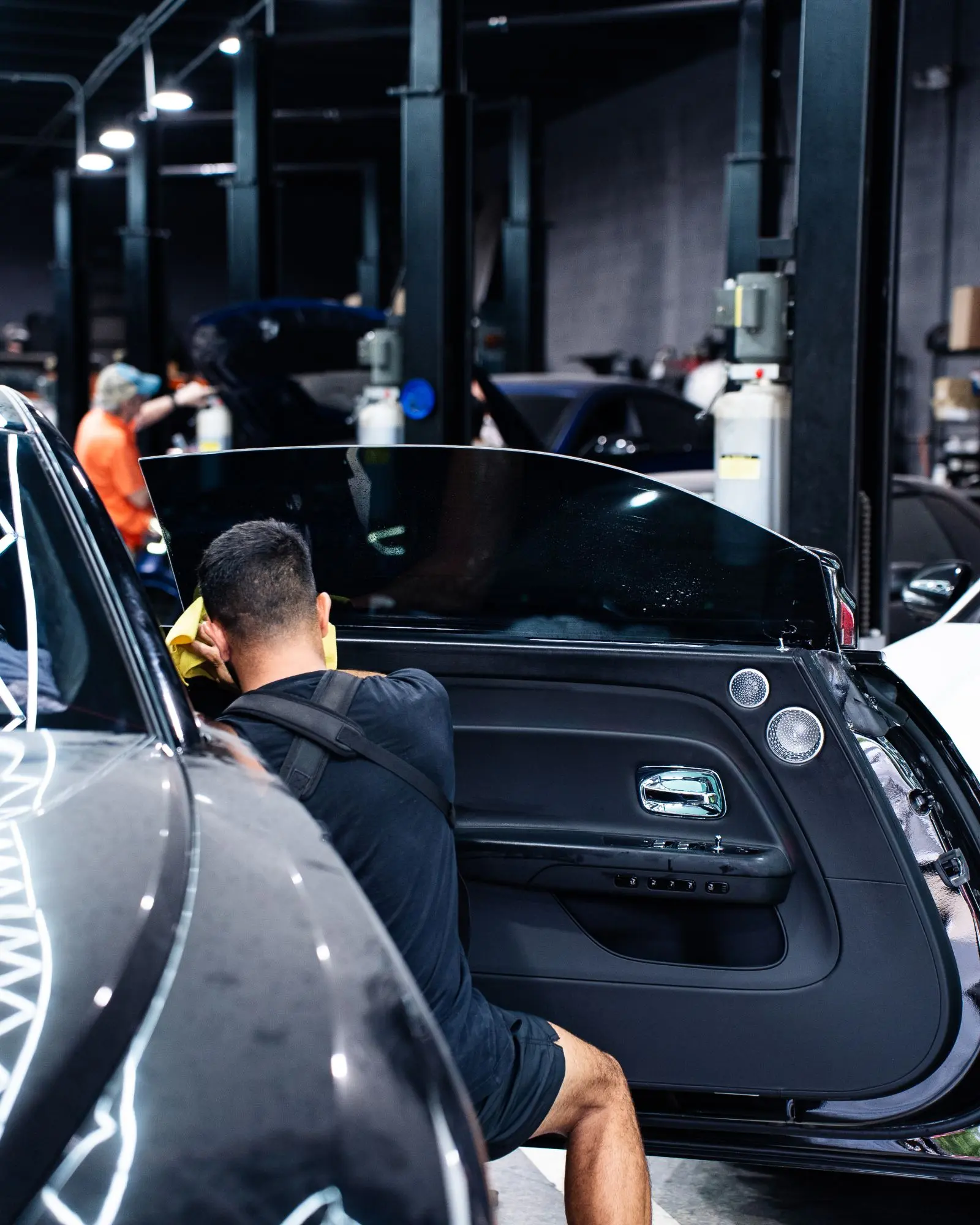 Technician wiping the freshly tinted door glass of a black luxury coupe in the shop