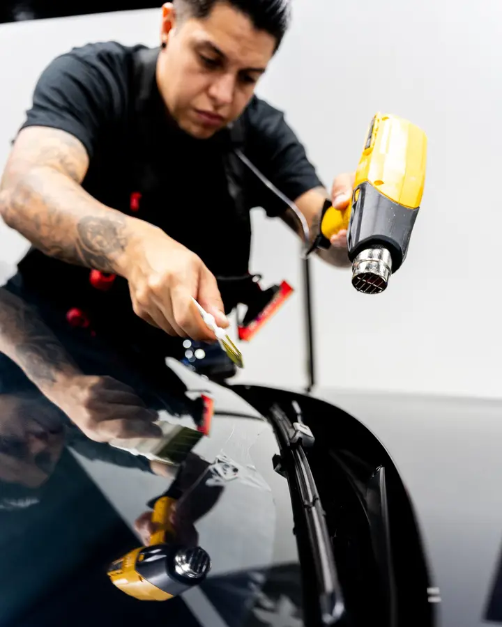 Technician using a heat gun and squeegee on film over a black car window