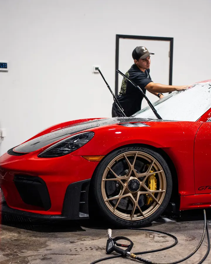 Technician foam washing a red Porsche sports car in the shop