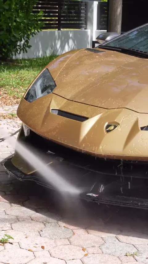 Technician washing a gold Lamborghini Aventador SVJ in a driveway