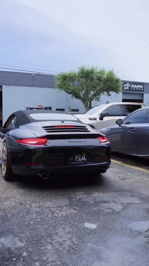 Technicians installing film on the side skirts of a black Porsche 911 cabriolet