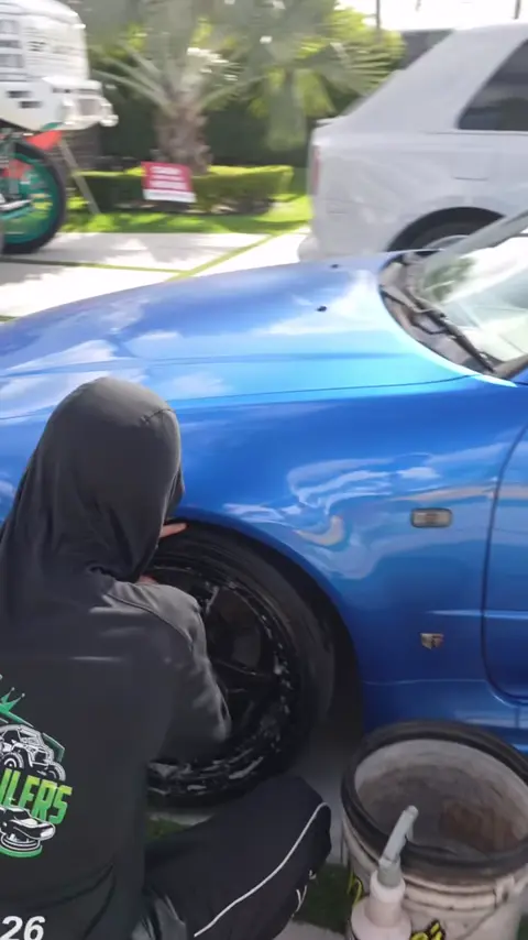 Technicians washing and detailing a blue Nissan Skyline GT-R in a driveway
