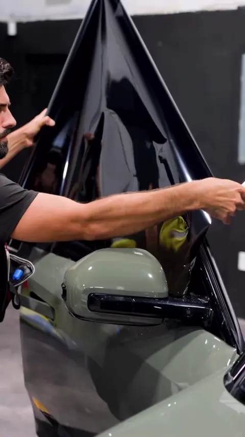 Technicians installing dark window tint on an olive green Rivian